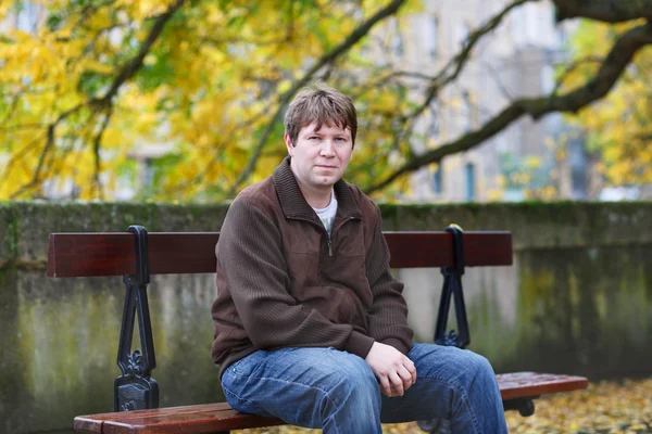 Πορτρέτο του όμορφο νεαρό άνδρα στο φθινόπωρο πάρκο κάθεται στο να — Φωτογραφία Αρχείου