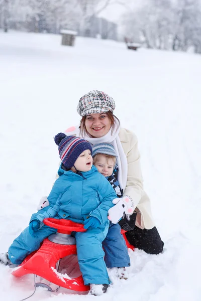 两个小的兄弟姐妹和他们的母亲在雪橇上赢开心 — 图库照片