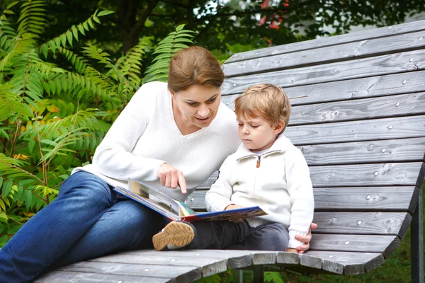 Little boy and his mother sitting on bench in park and reading b — Stock Photo, Image