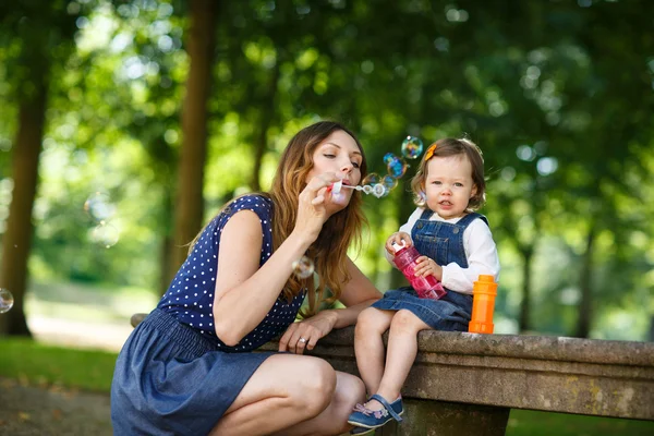 Beautiful mother and little daughter blowing soap bubbles in sum — Stock Photo, Image