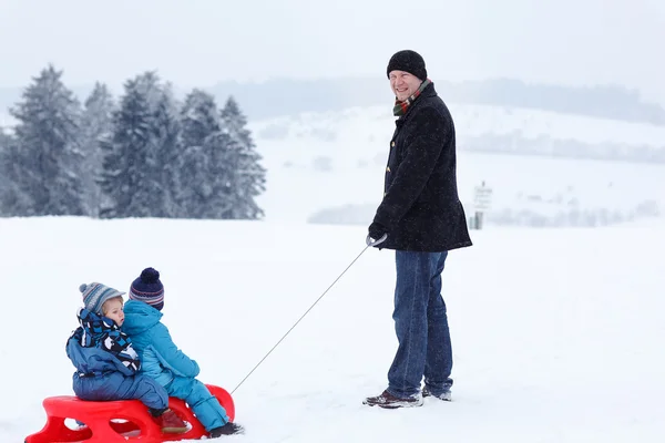 Two little siblings and their father having fun on sledge on win — Stock Photo, Image