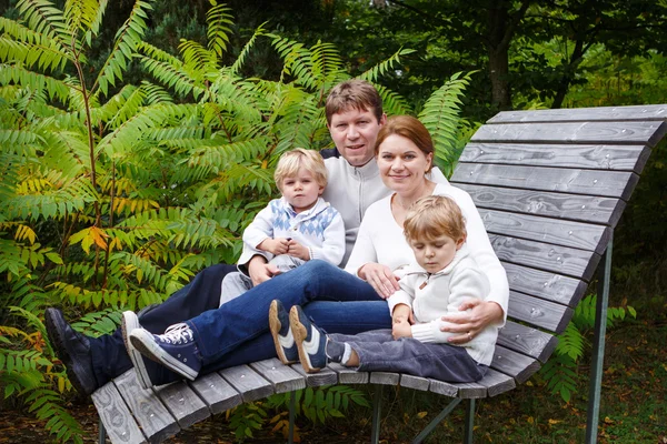 Famille de quatre personnes assise sur un banc dans un parc d'automne — Photo