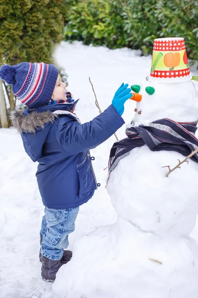 Adorable toddler boy having fun with snowman on winter day — Stock Photo, Image