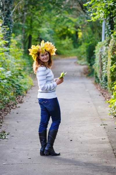 Glückliche junge Frau mit herbstlichem Ahornblätterkranz im Park. — Stockfoto