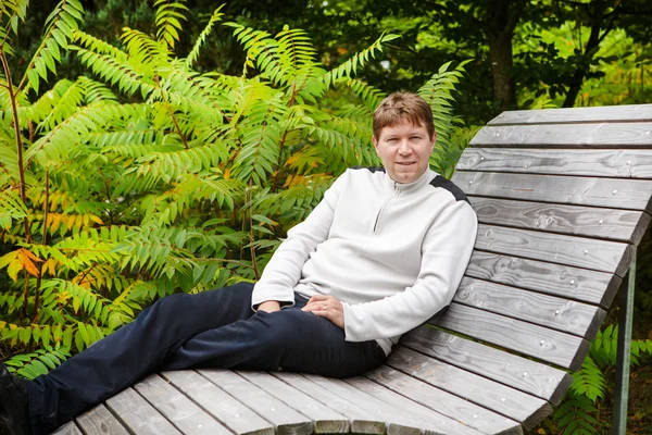 Porträt eines schönen jungen Mannes im herbstlichen Park sitzt auf sein — Stockfoto