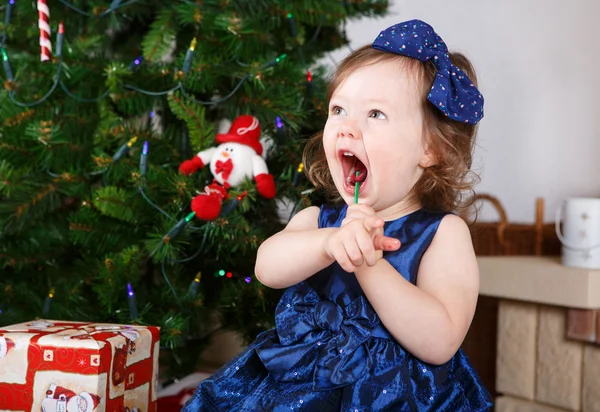 Little girl with lollipop and Christmas tree and decoration — Stock Photo, Image
