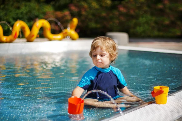Lindo niño jugando con agua junto a la piscina al aire libre — Foto de Stock