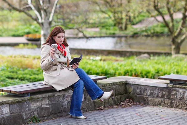 Young woman reading book and drinking coffee in spring park. — Stock Photo, Image