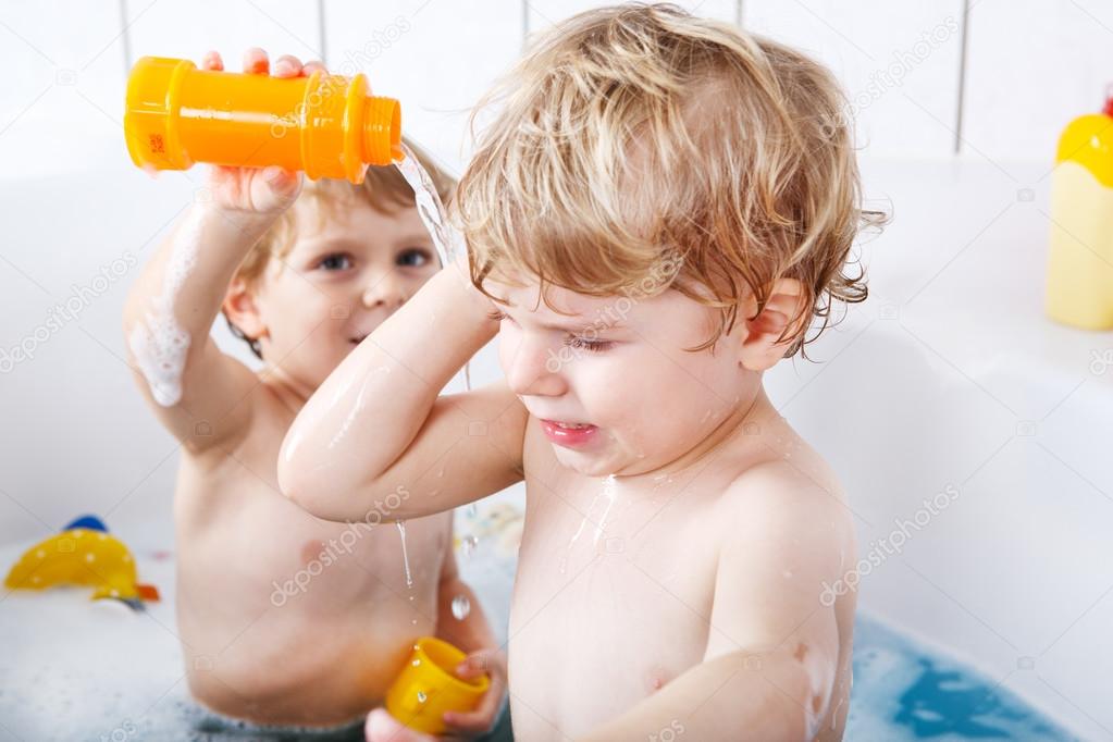 Two little twins boys having fun with water by taking bath in ba