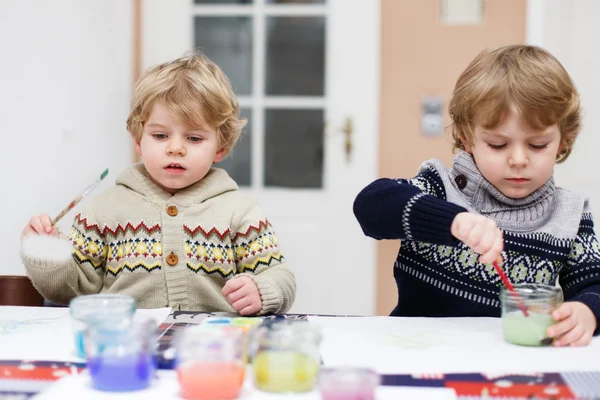 Dos niños gemelos divirtiéndose en interiores, pintando con diferentes —  Fotos de Stock