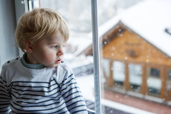 Pequeño niño mirando por la ventana en el día de invierno con — Foto de Stock