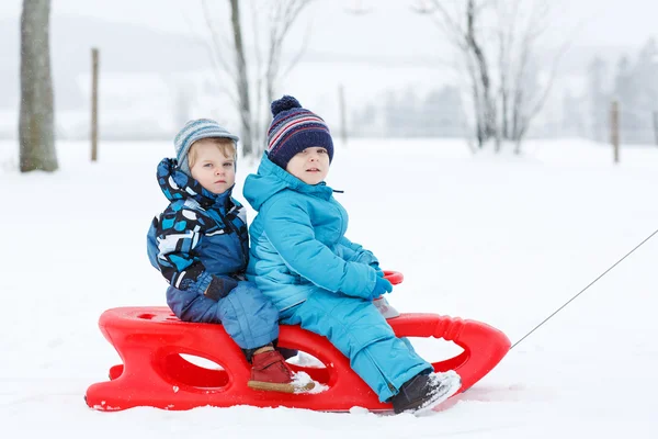 Двое маленьких братьев и сестер веселятся на санях в зимний снежный день — стоковое фото