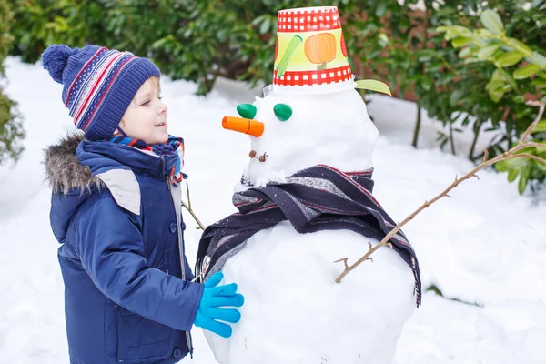 Adorable toddler boy having fun with snowman on winter day — Stock Photo, Image