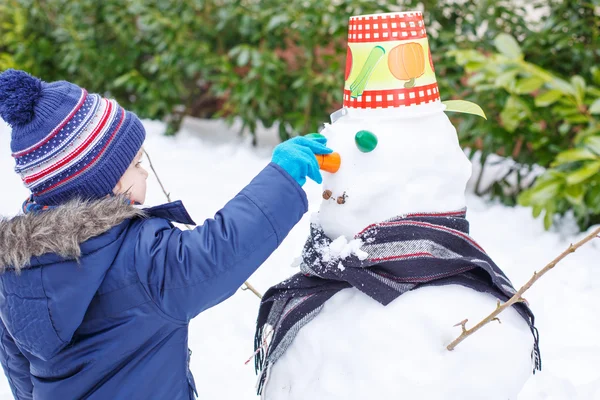 Adorable niño divirtiéndose con muñeco de nieve en el día de invierno —  Fotos de Stock