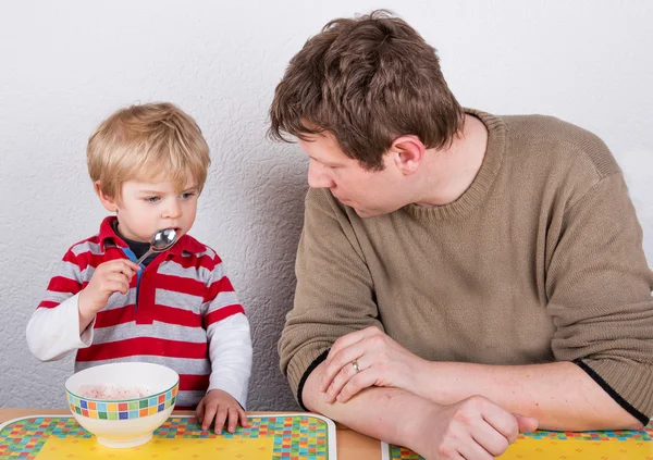 Jovem pai e pequeno filho comendo em casa cozinha . — Fotografia de Stock