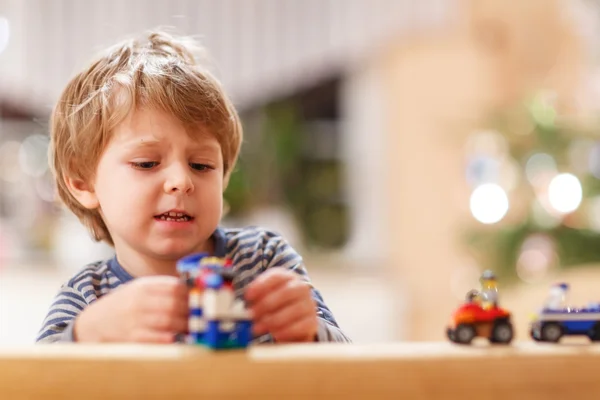 Pequeño chico rubio jugando con coches y juguetes en casa, interior . — Foto de Stock