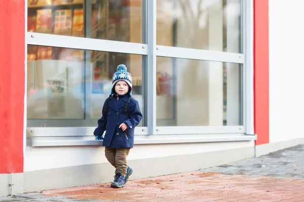 Petit garçon assis devant une grande fenêtre dans la ville, à l'extérieur , — Photo