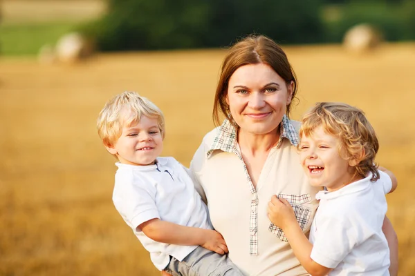 Молодая мать и два мальчика-близнеца веселятся на желтом сене — стоковое фото