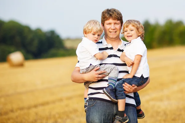 Joven padre y dos niños gemelos divirtiéndose en heno amarillo —  Fotos de Stock