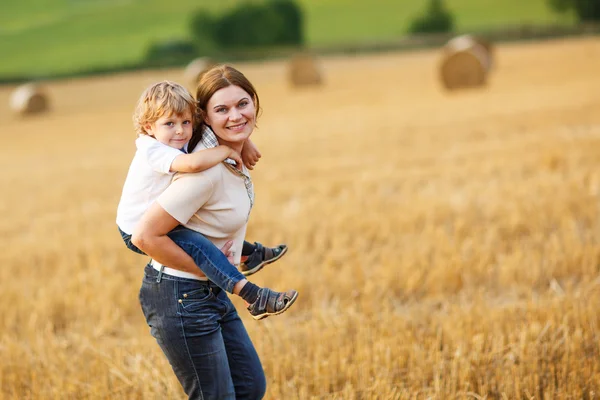 Young mother and her little son having fun on yellow hay field — Stock Photo, Image