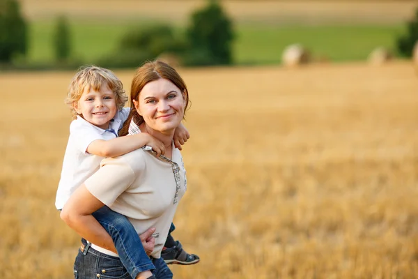 若い母親と幼い息子黄色干し草フィールド上で楽しんで — ストック写真