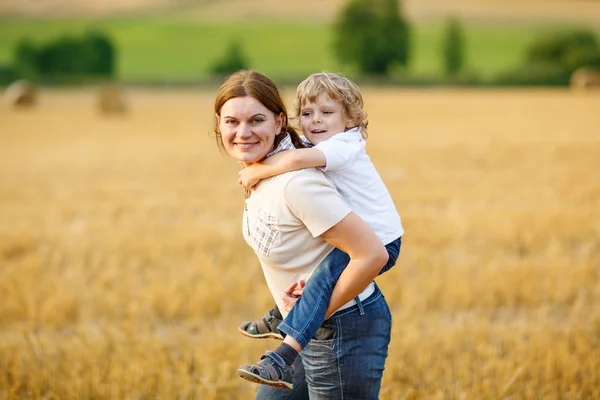 Young mother and her little son having fun on yellow hay field — Stock Photo, Image