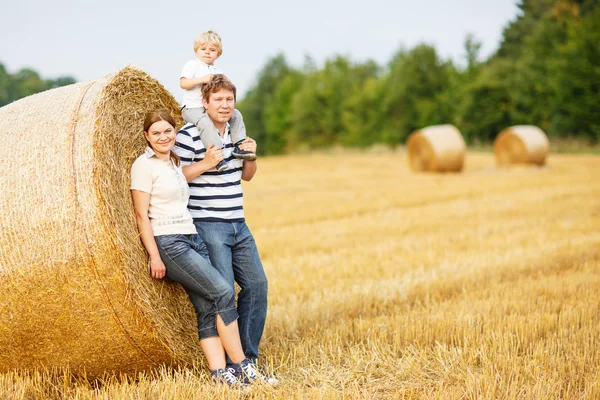 Glückliche dreiköpfige Familie auf gelbem Heufeld im Sommer. — Stockfoto
