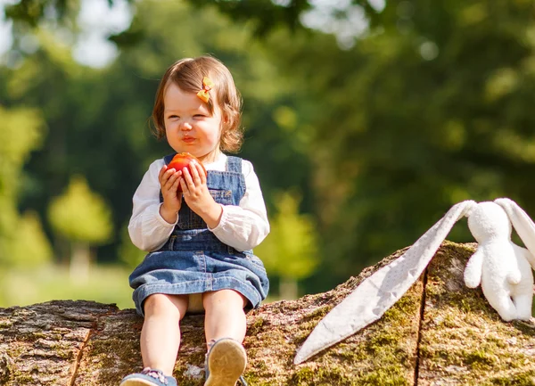 Little baby girl eating fresh apple in summer park. — Stock Photo, Image