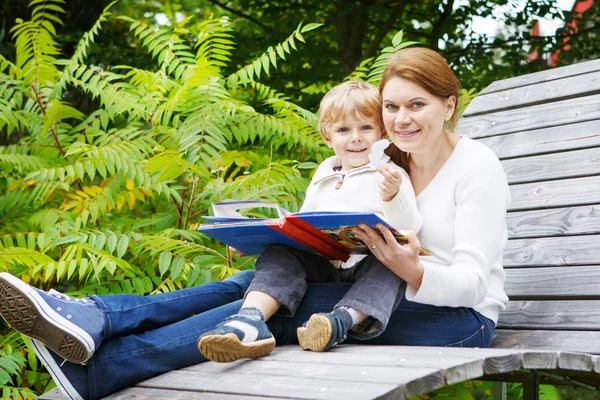 Kleiner Junge und seine Mutter sitzen auf Bank im Park und lesen — Stockfoto