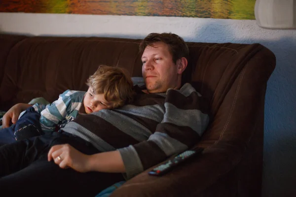 Милий маленький хлопчик і його батько дивиться телевізор, в приміщенні в темній кімнаті ввечері — стокове фото