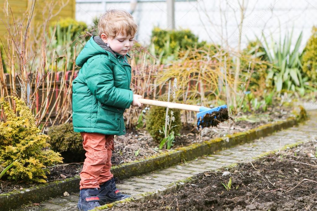 Little boy in spring with garden hoe, planting and gardening