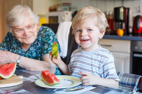 Kleine peuter jongen en zijn overgrootmoeder watermeloen eten een — Stockfoto