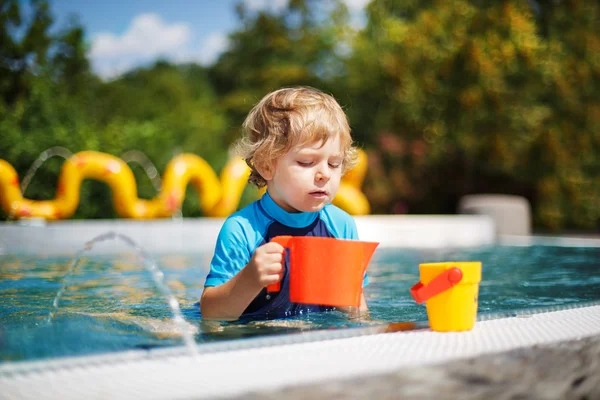 Lindo niño jugando con agua junto a la piscina al aire libre — Foto de Stock