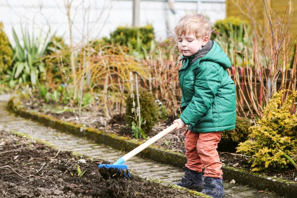 Kleine jongen in het voorjaar met tuin schoffel, planten en tuinieren — Stockfoto