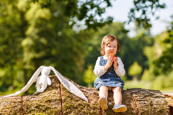 Liten flicka äter äpple i sommaren park. — Stockfoto