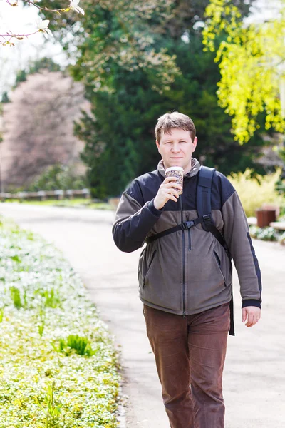 Jonge man wandel- en drinken koffie in park met bloeiende whi — Stockfoto