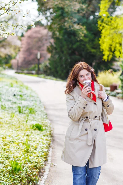 Jonge vrouw lopen en drinken koffie in park met bloeiende w — Stockfoto