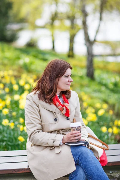 Jonge vrouw lezen van boek en drinken koffie in voorjaar park. — Stockfoto