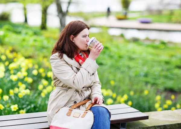 Молодая женщина читает книги и пьет кофе в весеннем парке . — стоковое фото
