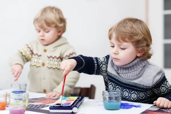 Dois pequenos gêmeos meninos se divertindo no interior, pintando com diferente — Fotografia de Stock