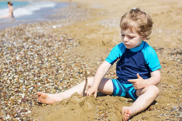 Little toddler boy playing with sand and stones on the beach — Stock Photo, Image