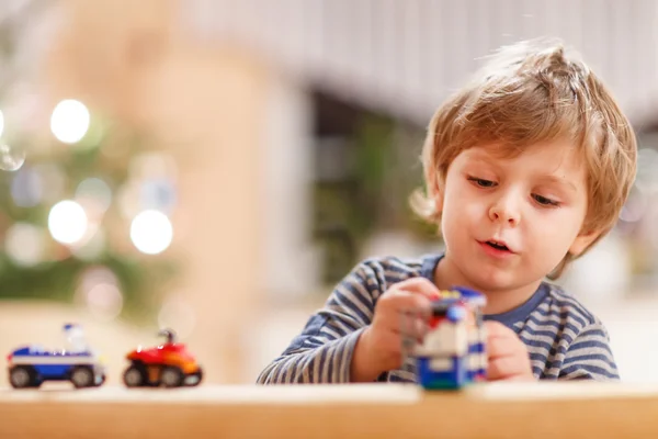 Piccolo ragazzo biondo che gioca con auto e giocattoli a casa, indoor . — Foto Stock