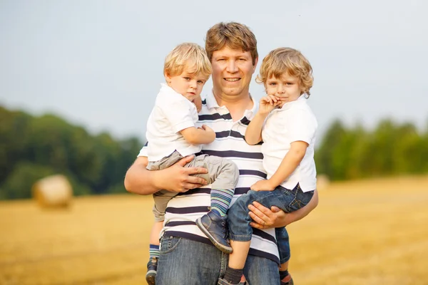 Junger Vater und zwei kleine Zwillingsbuben amüsieren sich auf gelbem Heu — Stockfoto