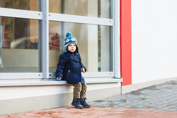 Kleine jongen zit infront van grote venster in de stad, buiten, — Stockfoto