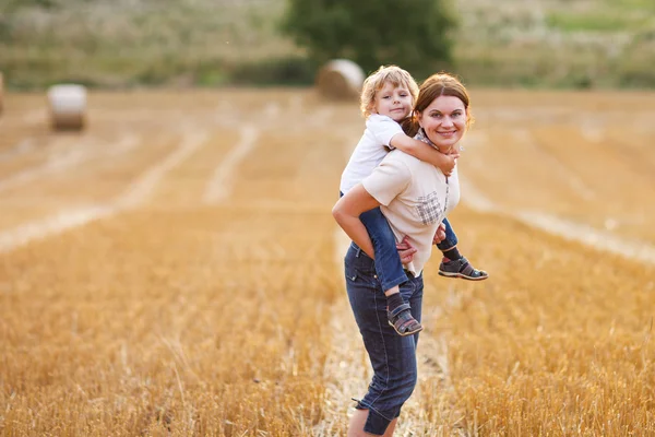 Young mother and her little son having fun on yellow hay field — Stock Photo, Image