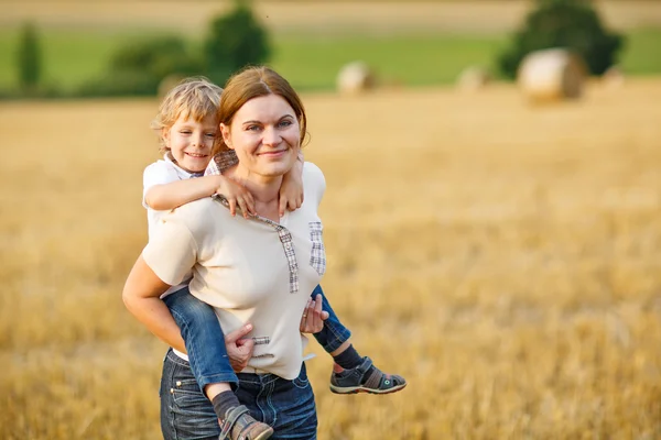 Young mother and her little son having fun on yellow hay field — Stock Photo, Image