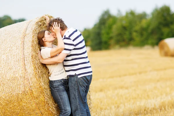 Young couple in love on yellow hay field on summer evening.