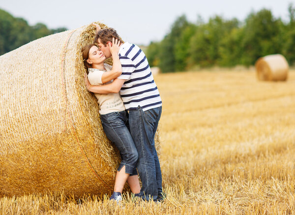 Young couple in love on yellow hay field on summer evening. 
