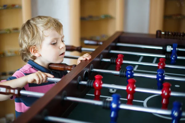 Küçük sarışın çocuk evde tahta masa futbol oynamak. — Stok fotoğraf