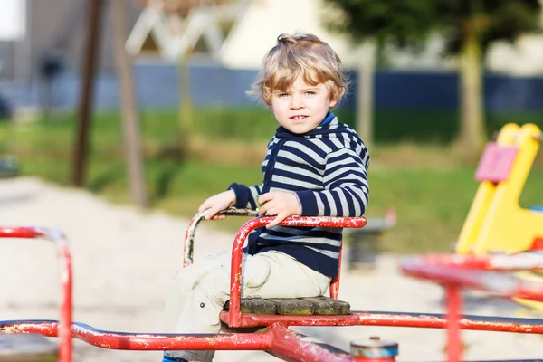 Pequeño niño divirtiéndose en el carrusel viejo en playgro al aire libre — Foto de Stock